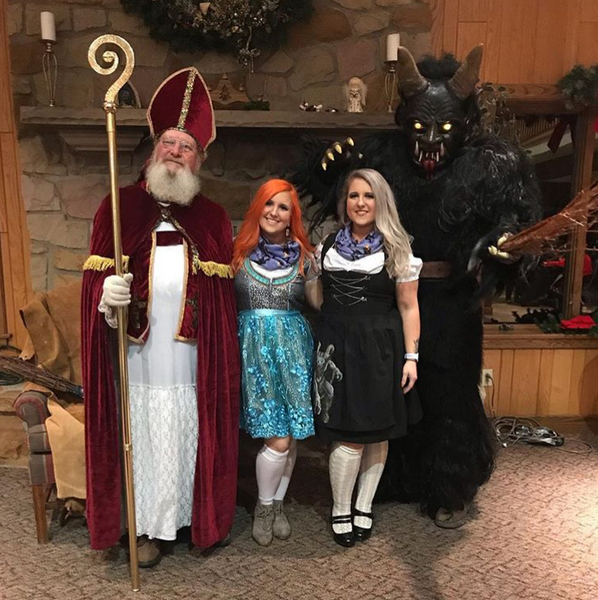 two women wearing dirndl dresses posing with st. nicholas and krampus at a german event