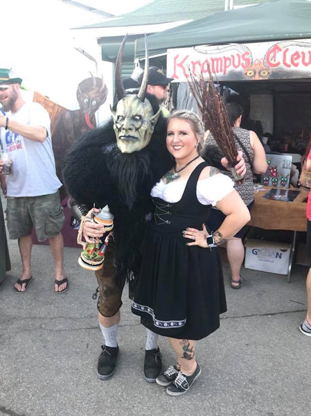 woman wearing a black dirndl dress posing with someone in a krampus mask at a krampuslauf