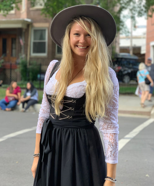 Woman with long blonde hair in a black Dirndl with a gray hat, smiling on a street in September