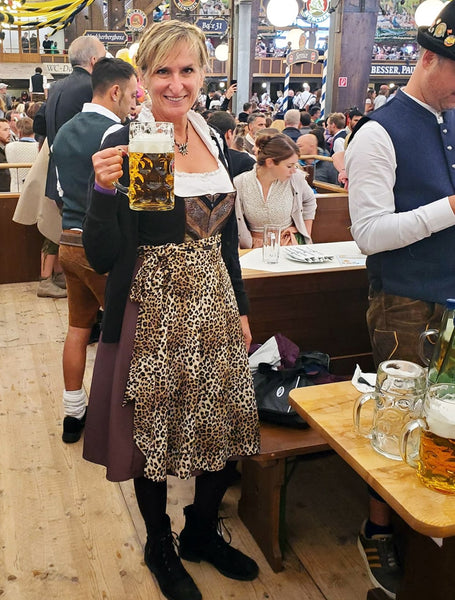 Woman wearing traditional German dirndl dress. With a white blouse and low neckline, black bodice and cheetah print apron. Holding a beer at Oktoberfest