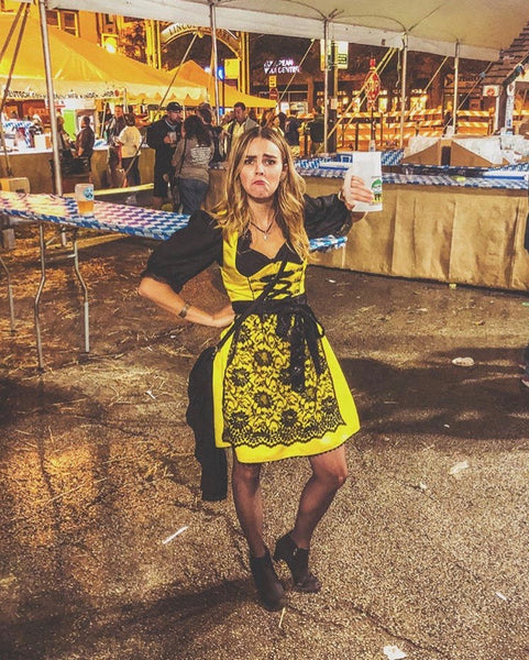 girl in a yellow dirndl dress with black lace dirndl apron and black blouse at Chicago Maifest with a sad face because her beer stein is empty