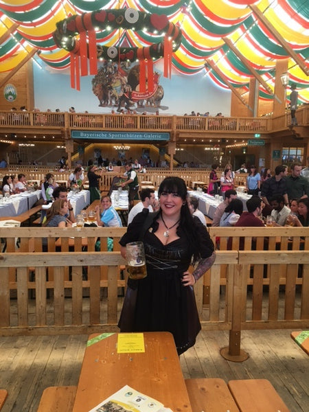 woman wearing a traditional bavarian costume or dirndl dress with black skirt smiling and holding a german beer in a beer tent at oktoberfest in munich