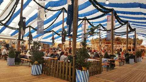 inside of the oktoberfest tents in the oide wiesn at oktoberfest in munich. Lots of picnic benches surrounded by small greenery and covered with a blue and white tent