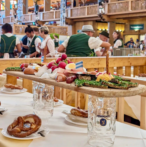 an oktoberfest charcuterie board on top of two empty glass beer stains in a beer tent. Oktoberfest foods to try