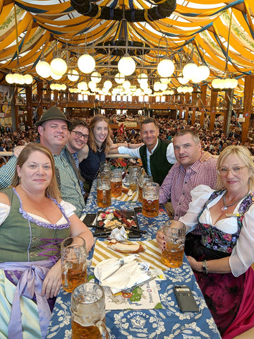 photo of a group of people wearing dirndl and lederhosen around a table at one of the tents at oktoberfest.