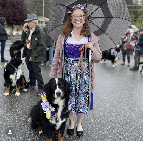 girl wearing a purple dirndl, floral dirndl apron, and blouse with her dog under an umbrella