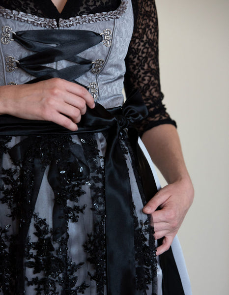 close up of a black lace dirndl apron with intricate handwork on a grey dirndl for oktoberfest