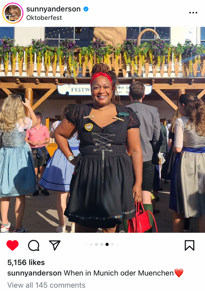 Food Network star, Sunny Anderson wearing a black dirndl dress at oktoberfest in munich with a red purses and red headband