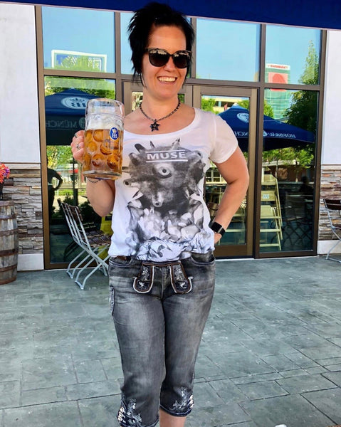 Woman, smiling, and standing in front of the Hofbrauhaus, with denim lederhosen with a drink