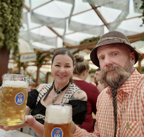 Couple wearing dirndl and lederhosen holding a stein of beer during the first weekend of oktoberfest in munich