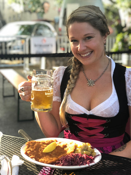 woman wearing a black dirndl dress with lace dirndl blouse wearing a schnitzel and holding a liter of beer