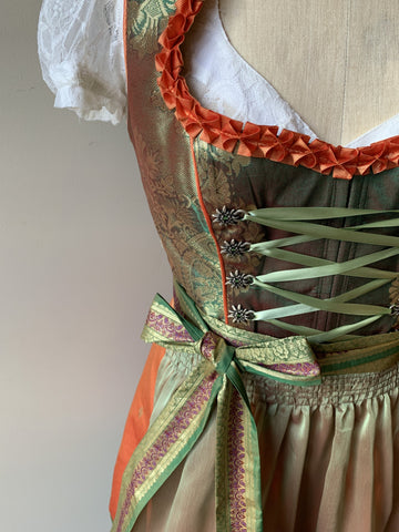 close up image of the custom made oktoberfest dress using an indian sari. it has orange trim around the tradition neckline, edelweiss hooks on the front, and a light green flowy apron. this is a beautiful custom oktoberfest costume