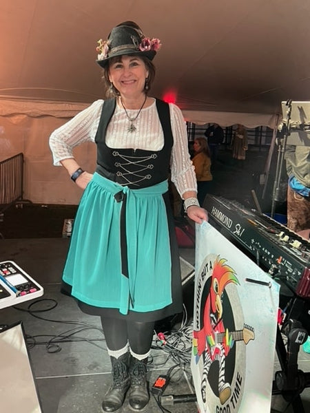Woman in a traditional german dirndl. Wearing a white blouse with long sleeved and a high neckline. The skirt is mid length, last her knees and worn with the bow in the front