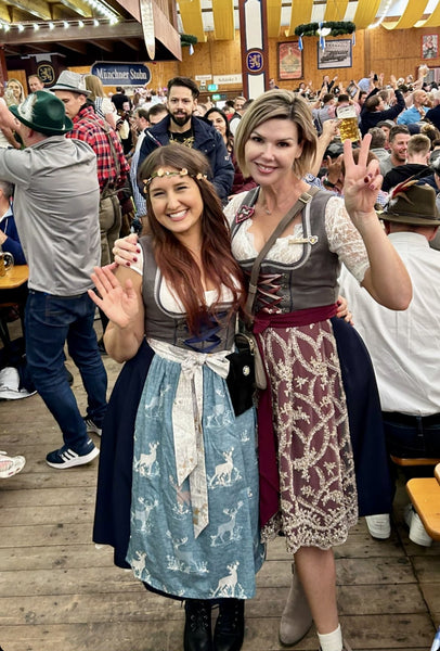 Two women wearing traditional dirndls, smiling inside one of the beer halls during a perfect oktoberfest trip