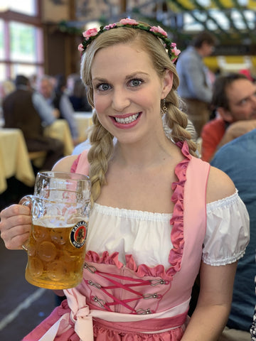 woman holding a liter of beer in a pink dirndl dress with braided hair in a beer tent at Maifest