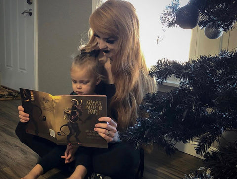 woman reading a krampus book to her daughter in front of a christmas tree