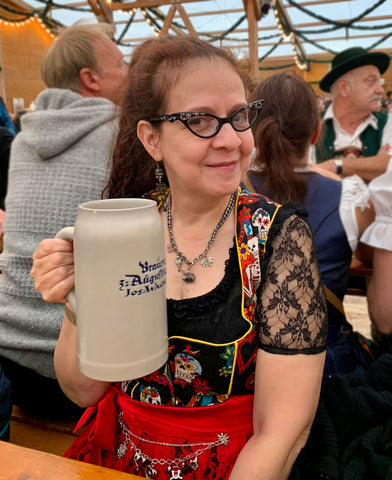 Maria at oktoberfest wearing a black and red dirndl and black dirndl blouse holding a liter of beer in an oktoberfest beer tent