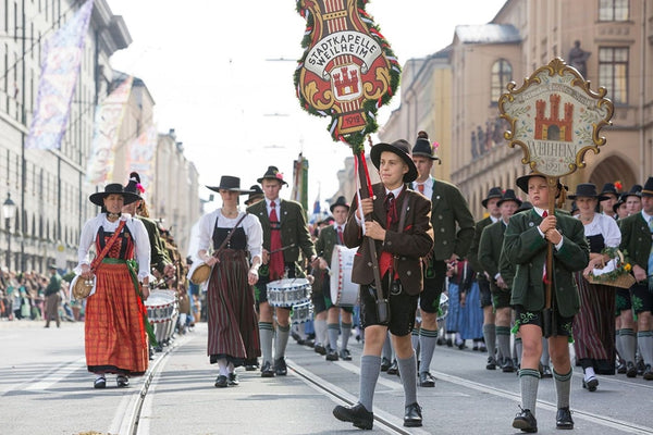 Group of people wearing traditional Bavarian costumes in the Oktoberfest parade. Young boy in the center, wearing knee length socks in lederhosen, holding a sign.