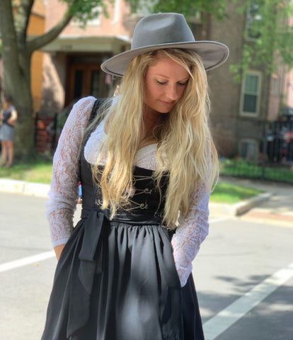 woman with long blonde hair and grey hat wearing a black dirndl dress for a German festival in chicago