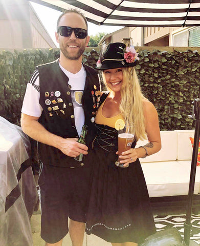 man in a German soccer jersey standing with a woman wearing a black dirndl dress with a Bavarian style hat