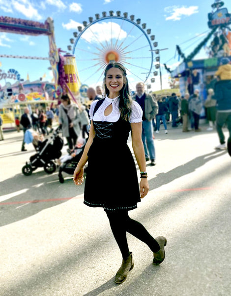 Smiling person wearing a black dirndl at Oktoberfest in front of a ferris wheel 