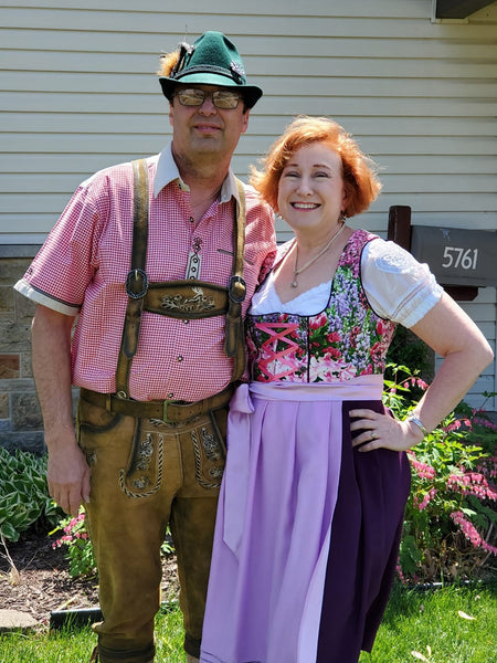 Man in Lederhosen and lady in dirndl standing in front of a home.