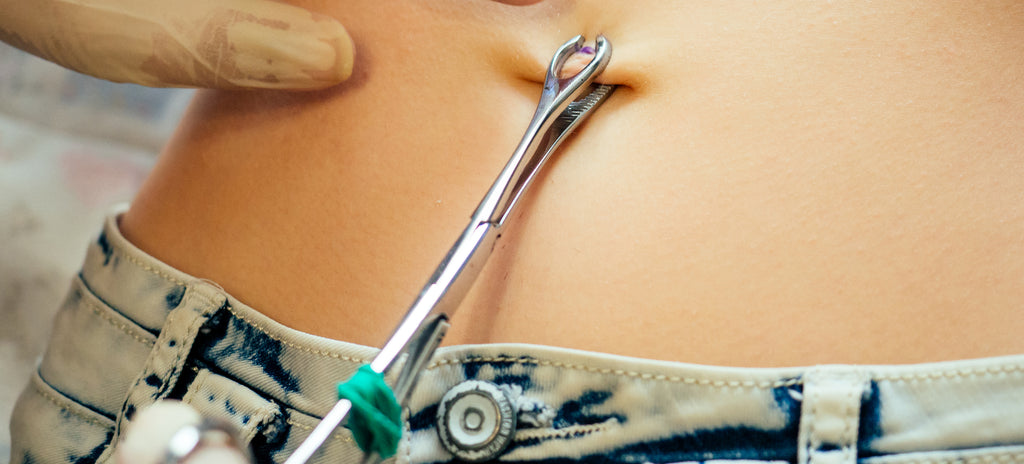 A close up of a women undergoing a belly button piercing with a licensed piercing professional.