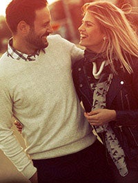 Man in white sweater stares while smiling at Woman with blonde hair smiling at man