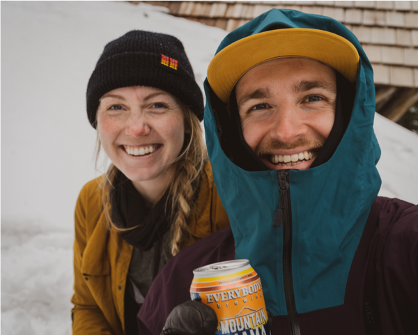 two backcountry skiers share a beer on a snowy summit
