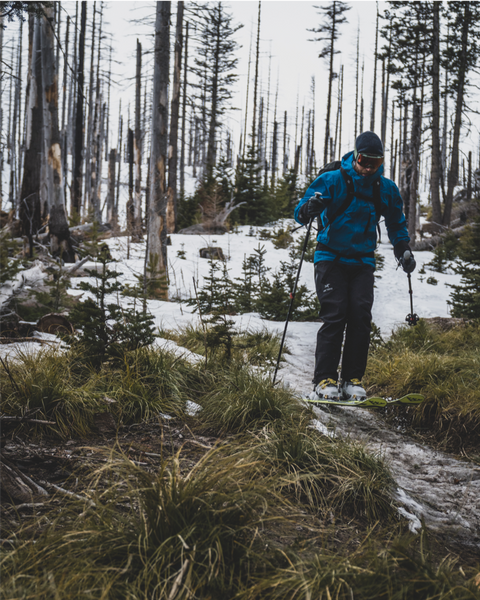 a backcountry skier skis a thin strip of snow on a muddy trail