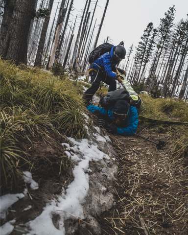 two backcountry skiers help one another stand in the mud