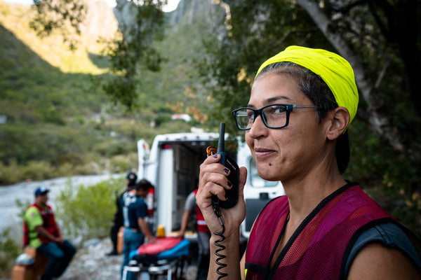 A woman stands near an ambulance, using a Rocky Talkie handheld radio to communicate with rescuers. 
