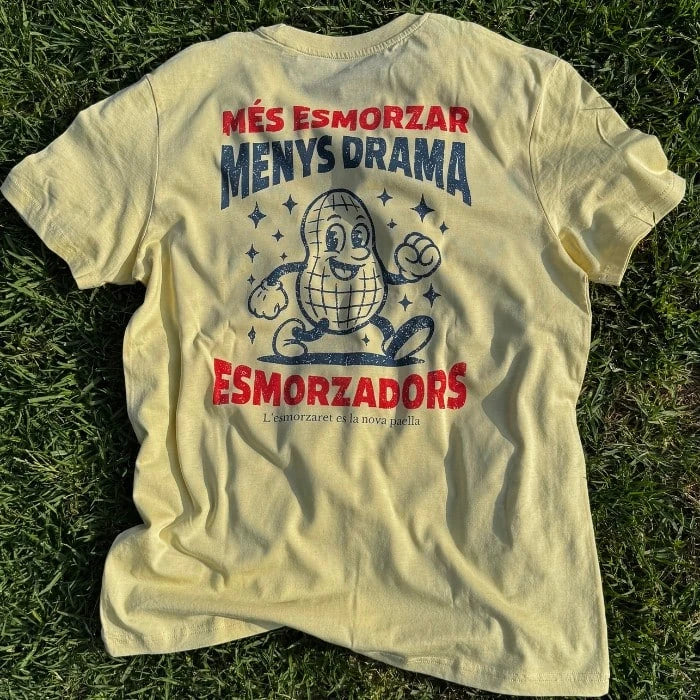 Camiseta amarilla de manga corta en la que sale un cacahuete andando y el mensaje "Més esmorzar menys drama"