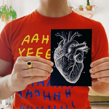 Chica sujetando entre las manos una tarjeta de color negro con un corazón anatómico blanco