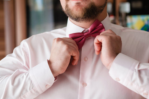 A man in a white shirt tying a red bow tie