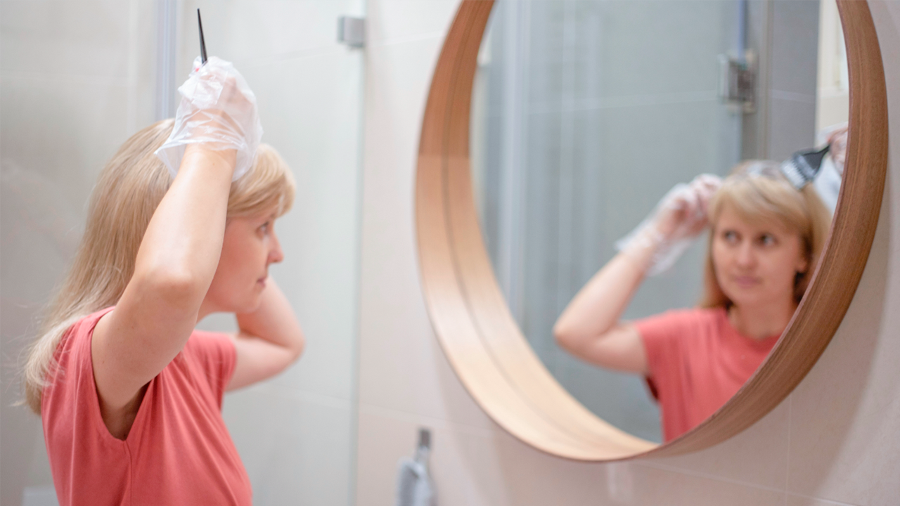 Como pintar cabelo em casa: mulher em frente ao espelho retocando a tintura
