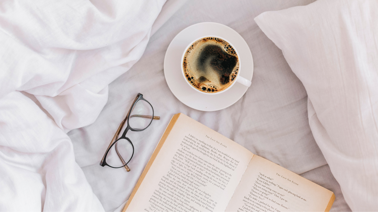 Livro e café ao lado de um óculos na cama