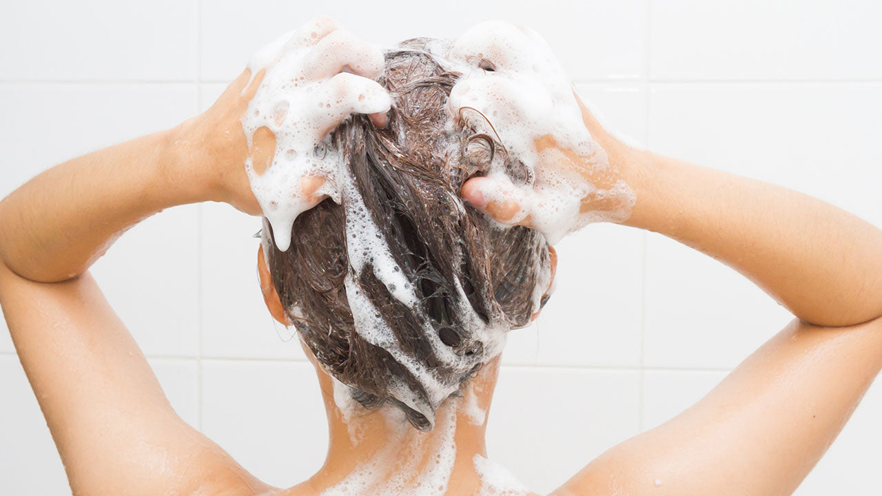 Mulher lavando o cabelo usando um shampoo com sulfato