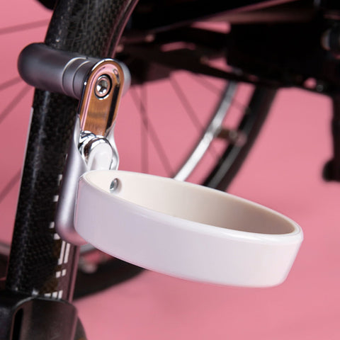 The FFORA CupHolder is attached to the lower tube of a wheelchair on a pink background.