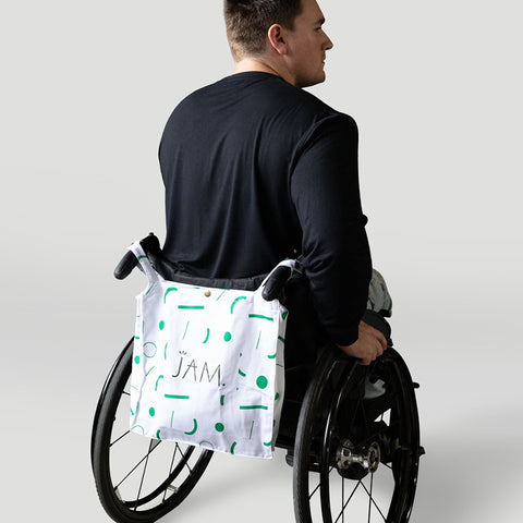  A man in a wheelchair from behind with white with green squiggles tote bag hanging from by double straps from handles.