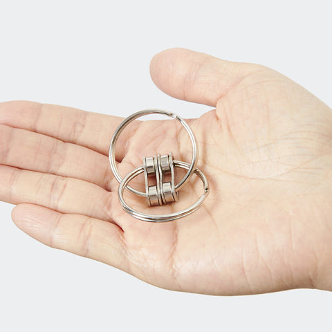 The Loop Fidget by Kaiko has two interlocking metal rings in a palm centred on a grey background.