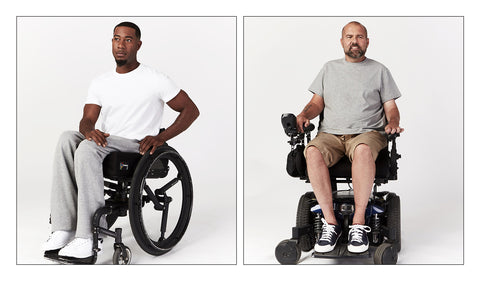 Man in wheelchair wearing Short Sleeve Open Back Tee and grey track pants in front of an off-white background. Second man is wearing the grey shirt in a power wheelchair. 