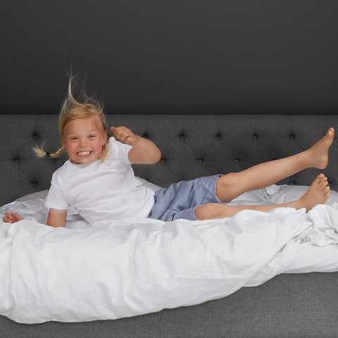 Alt text: a young child jumping on the bed wearing charcoal coloured Pjama Bedwetting Treatment pants.