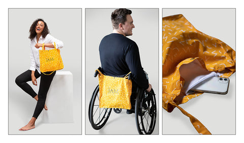  First image is a woman holding the mango coloured tote with JAM the label centred across the forearm highlighting the double straps. Middle image is the back of a man using a wheelchair with the tote bag hanging. Third image is a close up of the tote bag. 