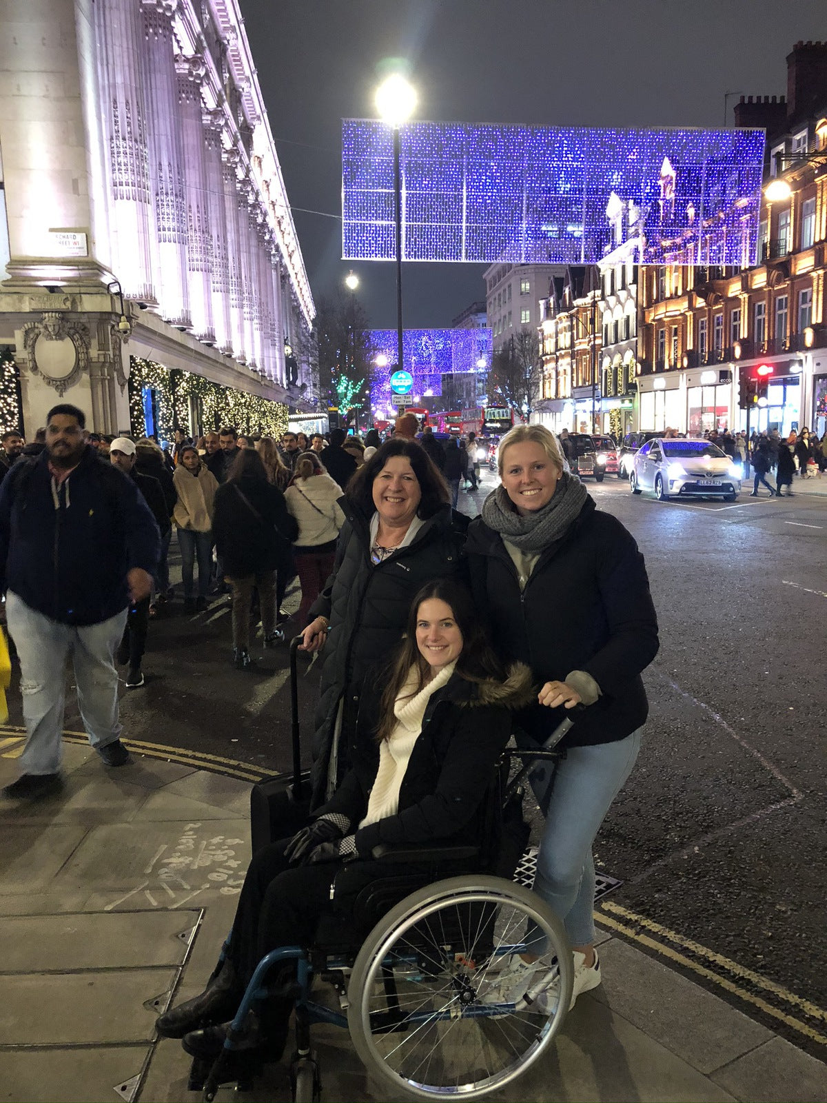 Alt text: Sarah sitting in her wheelchair, enjoying a night out on the town with family and friends.