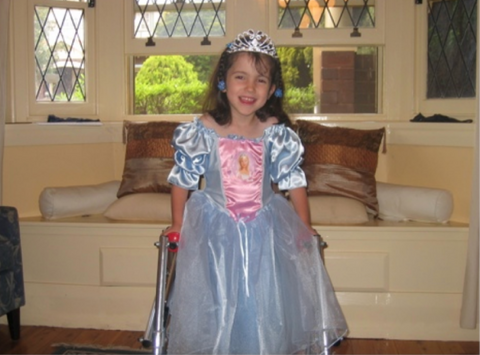 Alt text: Hannah standing with a walker fully dressed in her Princess gown of light blue and pink. Completing the outfit with her tiara.