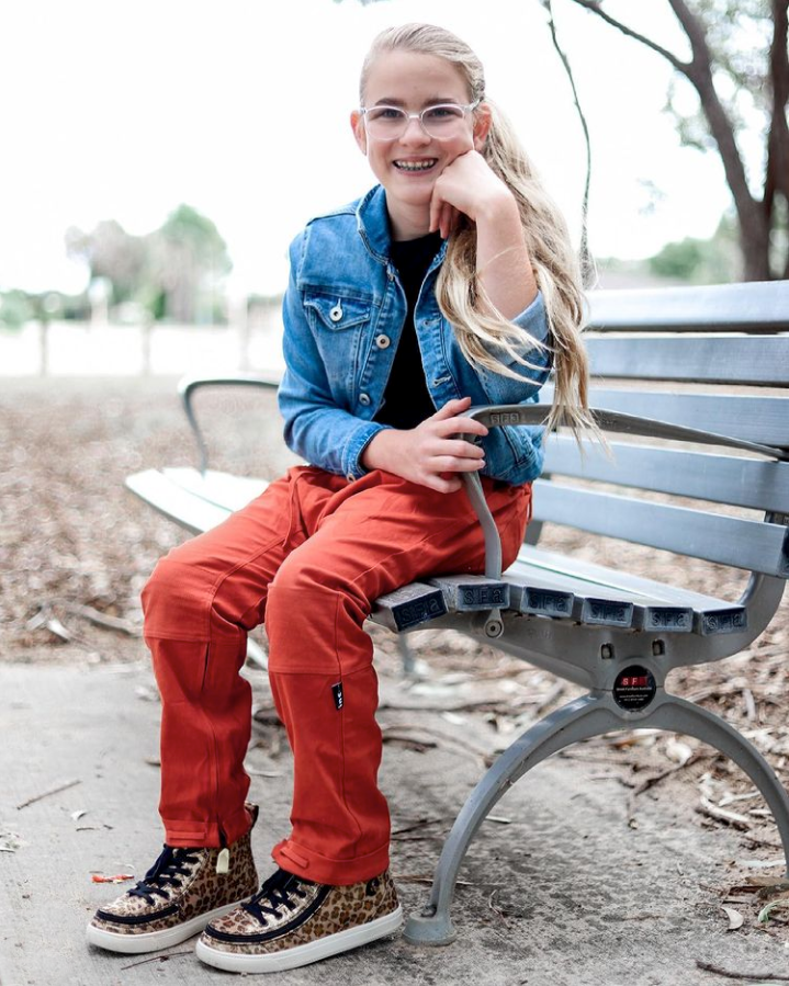 Alt text: Emily sitting on a park bench wearing Billy Footwears Classic Hi-Top sneaker in leopard print.