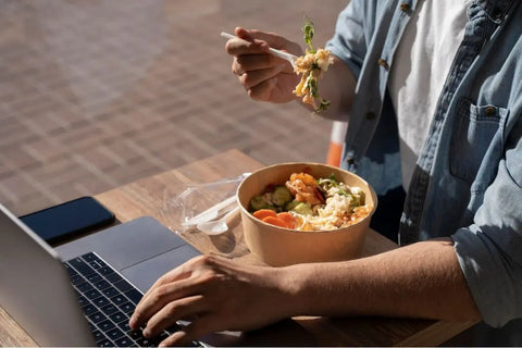 orang yang sedang makan sambil mengetik di laptop