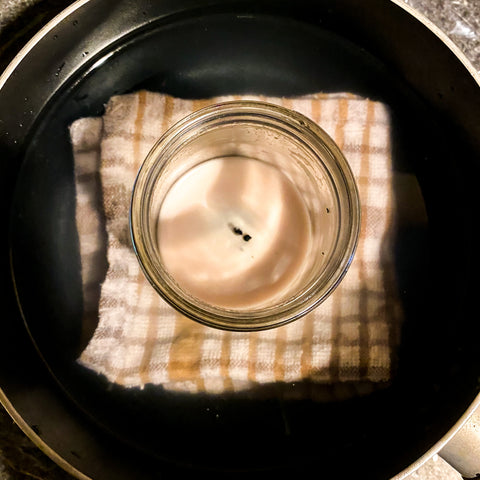 Candle sitting on a dish towel, inside a pot filled with water. This is the Marie Bain or Double Boiler Method of getting stubborn old wax out of candle jars. 