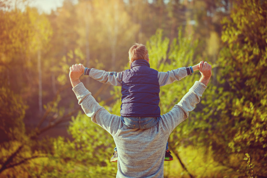 Father carries son on his shoulders in lush outdoor area